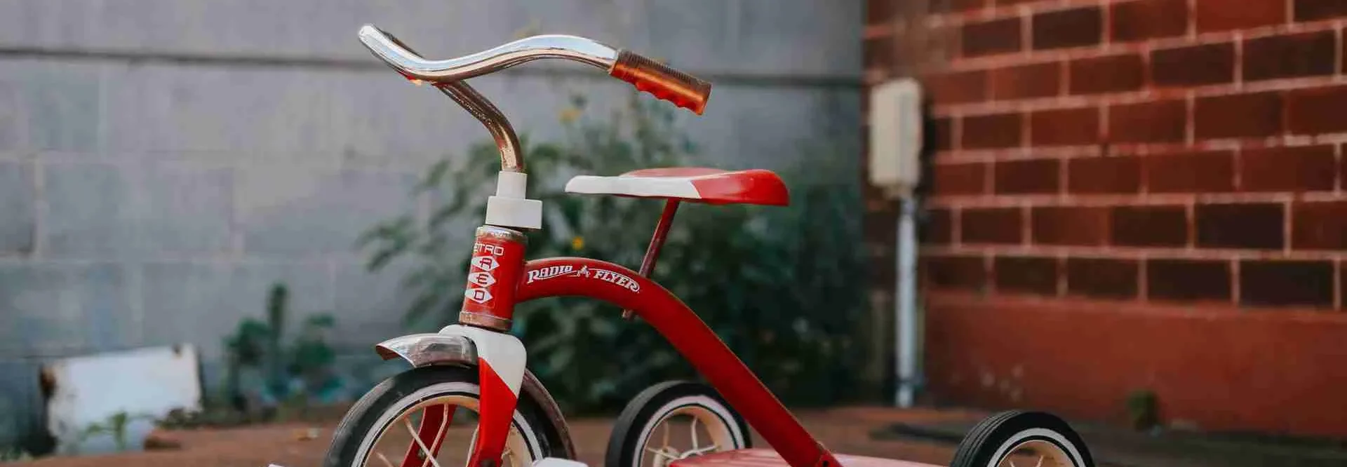 A red and white tricycle sitting in front of a concrete and brick wall.