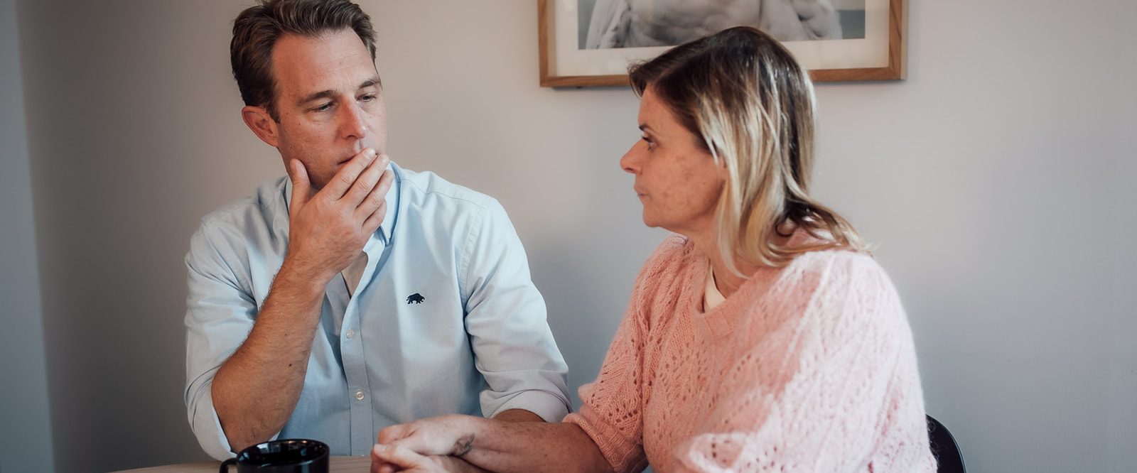 A man and woman sitting at a table drinking coffee, having a serious conversation.