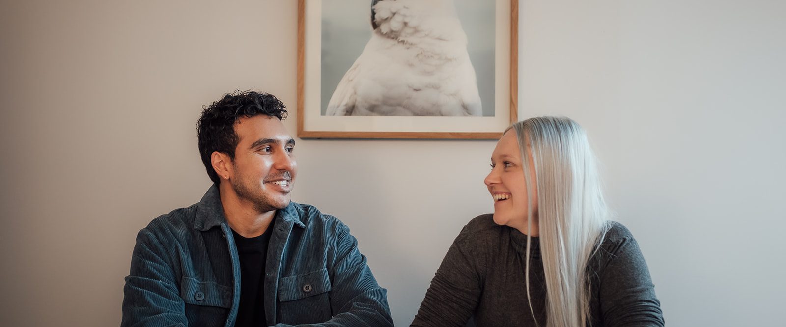 A man and woman sitting a table drinking coffee, talking and smiling.