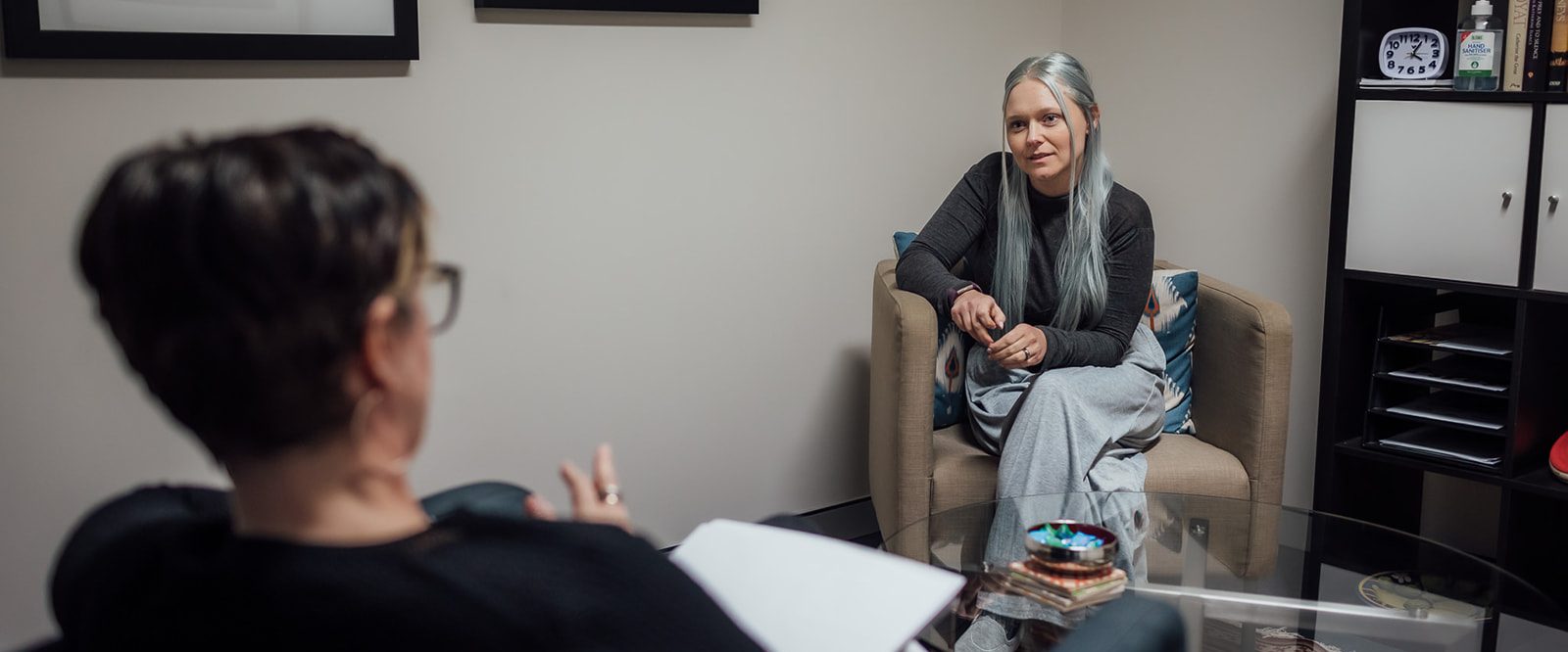 A young woman wearing a black jumper and long grey skirt sitting talking to a female counsellor.