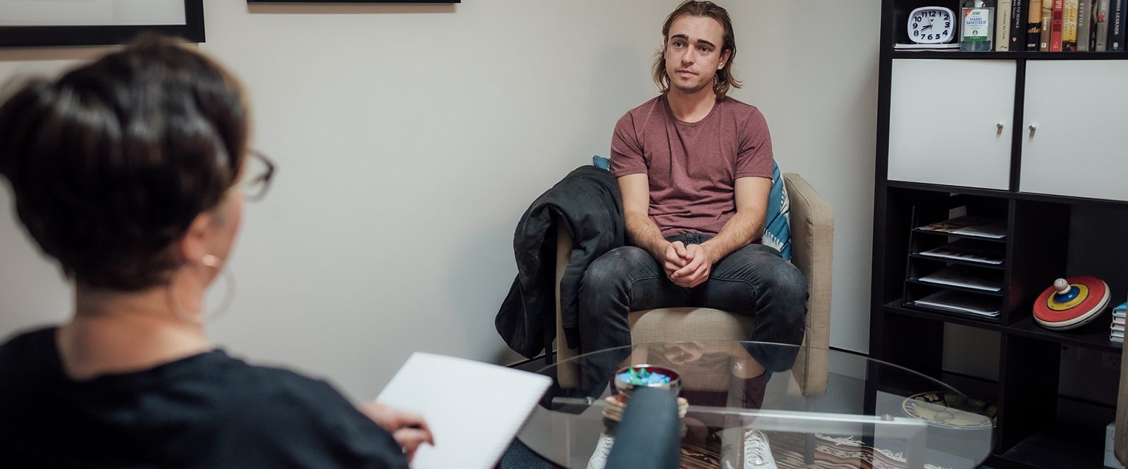 A young man sitting in a chair facing a woman with a notebook, talking.