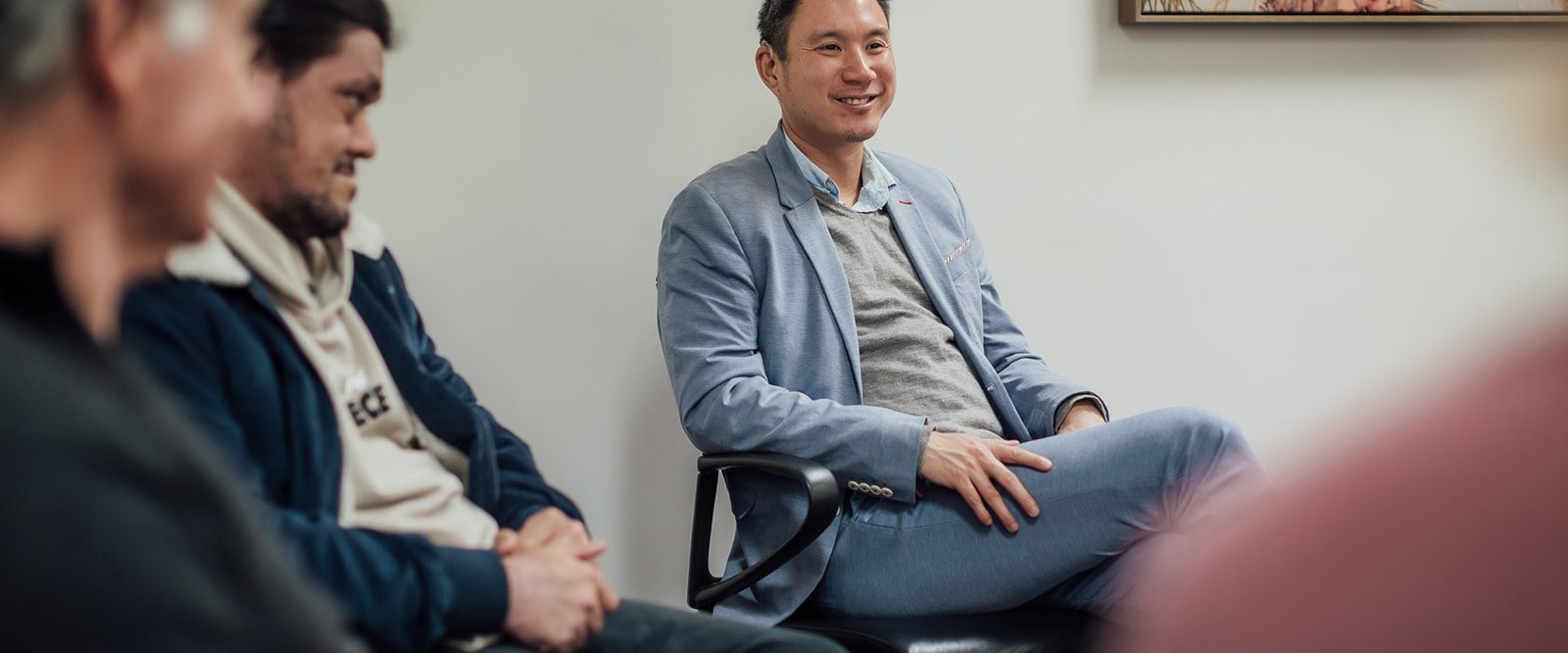 A man sitting in a group with two other men, talking and smiling.