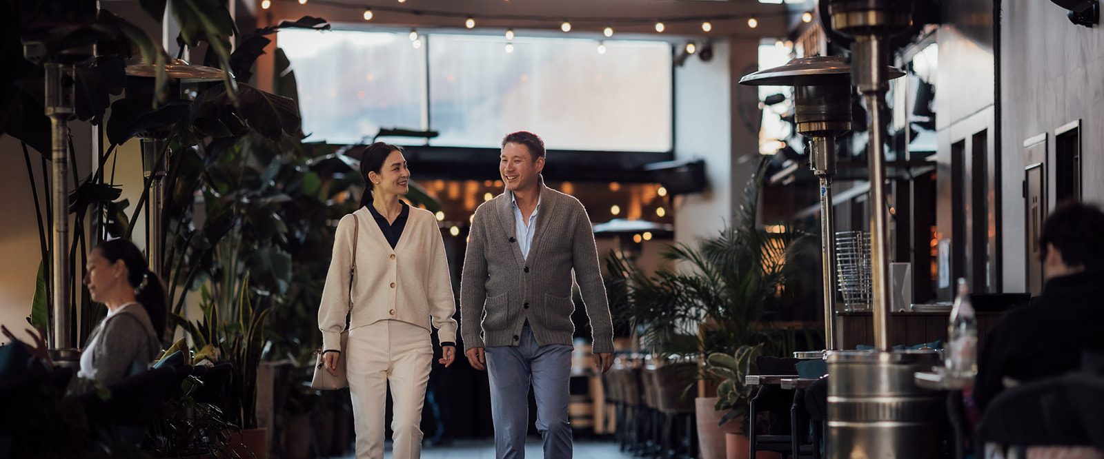 A man and a woman walking past restaurants, talking.
