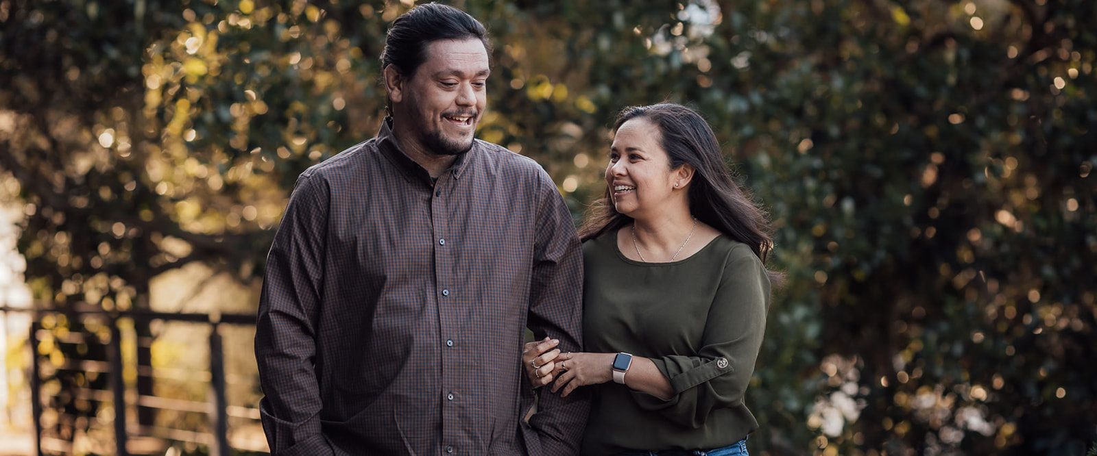 Couple smiling while walking arm in arm through a park.